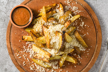Parmesan wedge fries with sauce on a cutting board