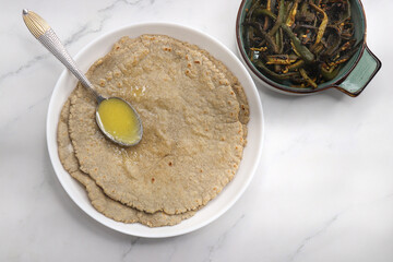 Jowar flour flatbread known as bhakar or jawari bhakri. served with ghee, spicy garlic or lasun chutney, bhindi or lady finger sabji. farmer's food. Maharashtrian village food. copy space.
