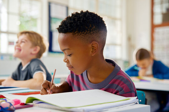 Black little child taking notes on notebook during lesson - Powered by Adobe