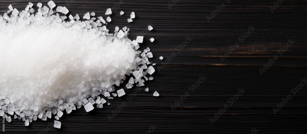 Poster close-up of white sea salt crystals scattered on a dark wooden surface with ample copy space for pro