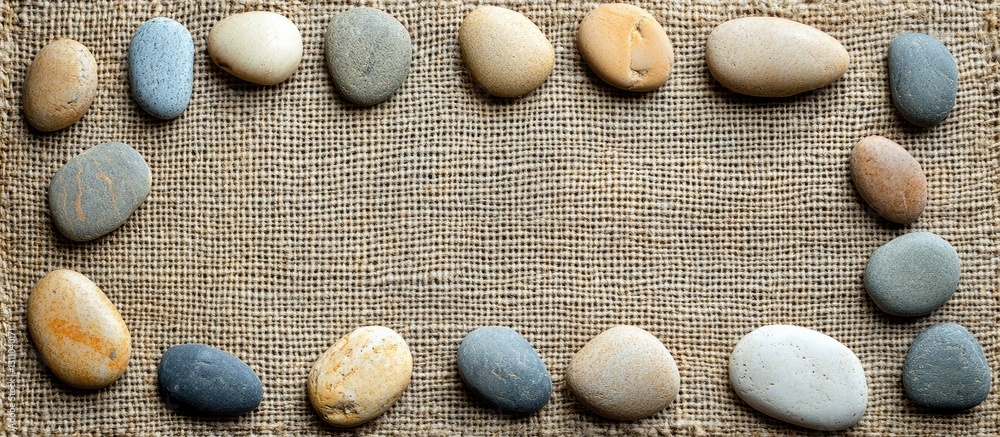 Aufkleber Natural arrangement of smooth pebbles in soft earth tones on textured fabric background, creating a serene framed scene for design or decoration.