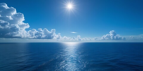 Obraz premium Breathtaking view of the deep blue ocean under a bright sun with scattered clouds on the horizon, creating a peaceful and relaxing seascape perfect for backgrounds and wallpapers