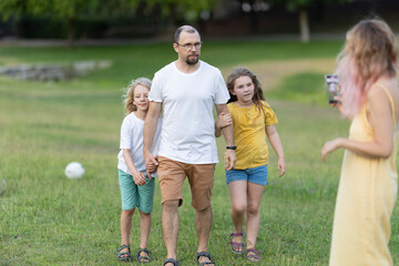Father walking with daughters in park while mother is filming