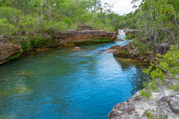The pristine water of Eliott Creek flows through rock formations and is surrounded by lush tropical...