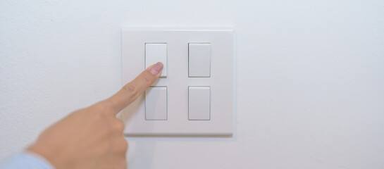 Female finger pushing for turn on light switch on white wall at home room. Woman hand turn off...