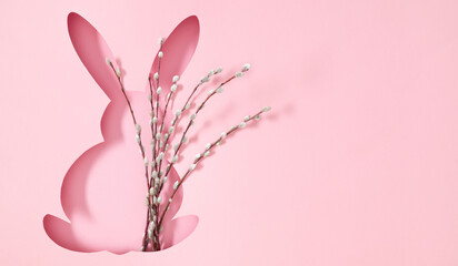 Bright image of silhouette of Easter bunny filled with blossom pussy willow branches on light pink background. Top view. Banner.