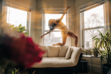 Woman dancing gracefully on a couch, illuminated by golden sunlight