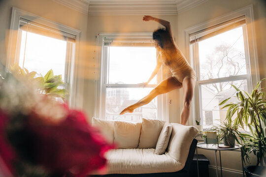 Woman balancing dynamically near a sunlit window in a graceful pose