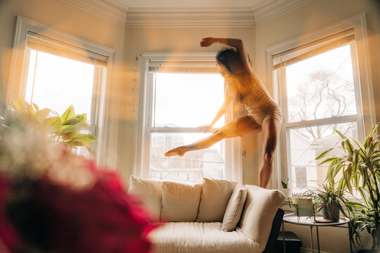 Woman balancing dynamically near a sunlit window in a graceful pose