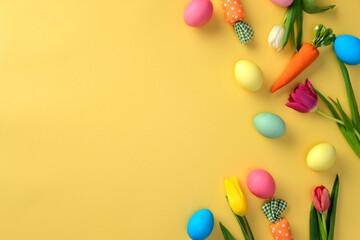 Happy Easter greeting card design. Top view colorful Easter eggs, decorative carrots and tulips on yellow background