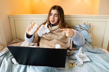 Sick young woman consulting seeking advice online doctor via laptop while holding various...