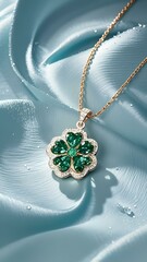 A stunning image showcases a gold necklace with a clover - shaped pendant set with vivid green gemstones, resting on a textured, light blue surface.