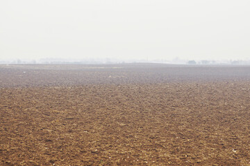 Obraz premium A field used for growing crops after digging. A landscape from the Serbian countryside: dug up loose soil without weeds or plantings and a foggy forest on the horizon. Spring work in the village.