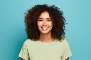 Fototapeta premium A young woman with curly hair beams with happiness, radiating joy in front of a bright blue backdrop. Her warm smile captures the essence of positivity and confidence in a casual environment
