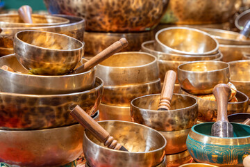 Variety of Tibetan singing bowls crafted from hammered brass and bronze stacked together featuring wooden strikers inside producing deep tones for meditation and relaxation