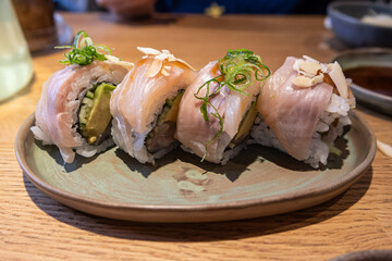 Delicious sushi rolls filled with fresh fish and avocado, sprinkled with sesame seeds and topped with passion fruit, presented on a ceramic plate