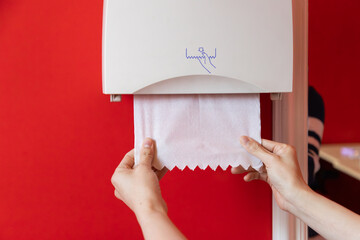 A person is holding a roll of toilet paper in front of a dispenser