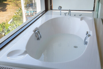 A large white bathtub with a window above it