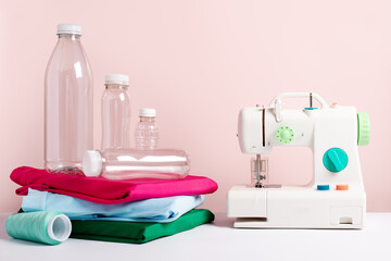 Plastic bottles, sewing machine and folded t-shirts still life on pink, concept of clothes made from recycled plastic