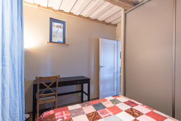 Cozy Home Bedroom Interor with Wooden Ceiling and Colorful Quilted Bedspread. Open Door