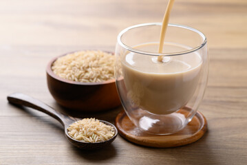 Organic rice milk pouring into cup glass on wooden background, Alternative milk made from plant