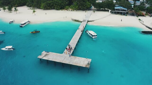 Aerial shot of the Maldives Fulidhoo inhabited island with sapphire waters and white speedboats picking up tourists at the T-shaped pier
