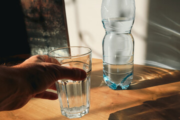 Hand holding drinking water bottle pouring into glass. Hand pouring water from bottle into a glass