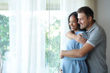 Happy interracial couple enjoying pregnancy looking away
