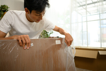 Happy young asian man unpacking and assembling furniture at home