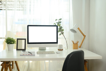 Desktop computer with blank screen, desk lamp, documents, coffee mug and decorative plants