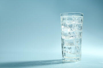Soda water with ice cubes in glass on light blue background, space for text