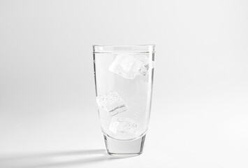 Refreshing soda water with ice cubes in glass on light grey background