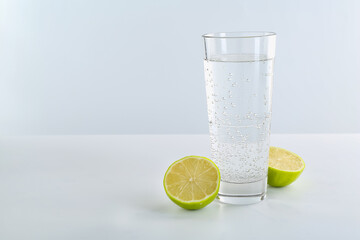 Refreshing soda water in glass and halves of lime on white table against light background. Space for text