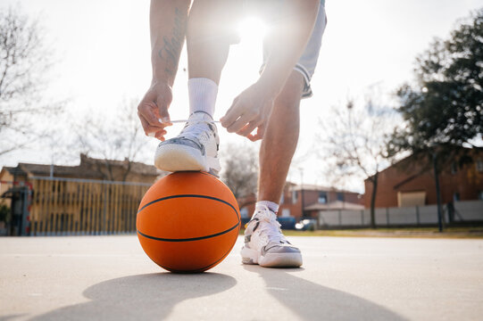 Basketball player tying shoelaces with ball on outdoor court