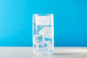 Refreshing soda water with ice cubes in glass on wooden table against light blue background, closeup