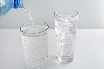 Pouring refreshing soda water into glass at white table against light background