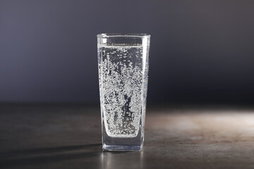 Refreshing soda water in glass on grey table against dark background, closeup