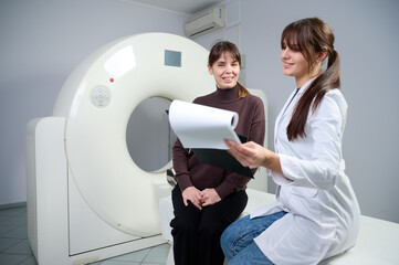 Radiologist showing x-ray report to the female patient. Confident pretty doctor consulting woman in...