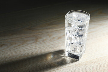 Refreshing soda water with ice cubes in glass on light wooden table, closeup. Space for text