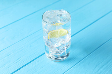 Refreshing soda water with ice cubes and slice of lemon in glass on light blue wooden table, closeup
