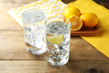 Refreshing soda water with ice cubes in glasses and lemons on wooden table, closeup