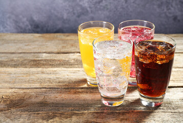 Soda water of different flavors with ice cubes in glasses on wooden table, space for text