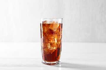Sweet soda water with ice cubes in glass on white wooden table