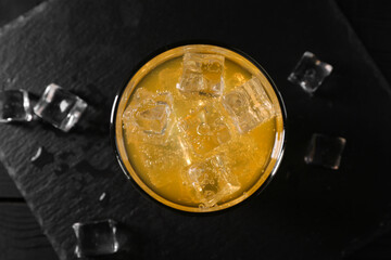 Sweet soda water with ice cubes in glass on black table, top view
