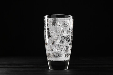 Refreshing soda water with ice cubes in glass on black wooden table