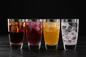 Refreshing soda water of different flavors with ice cubes in glasses on black wooden table