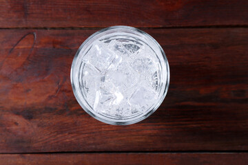 Refreshing soda water with ice cubes in glass on wooden table, top view