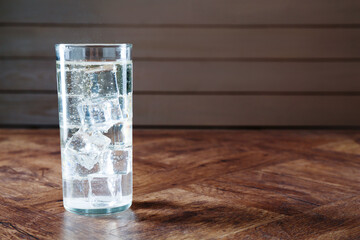 Refreshing soda water with ice cubes in glass on wooden table, space for text