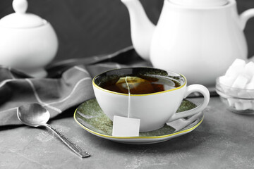 Tea bag in cup with hot drink, teapot and spoon on gray textured table