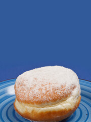 A close-up of a single doughnut sprinkled with powdered sugar, placed on a patterned blue plate